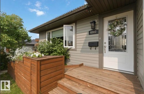 Entryway featuring a white paneled door with decorative glass, a dark exterior light fixture, and horizontal siding - 4007 45 Street, Stony Plain, AB 