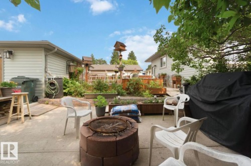 Concrete patio featuring a block fire pit, raised garden beds, and mature trees - 4007 45 Street, Stony Plain, AB 