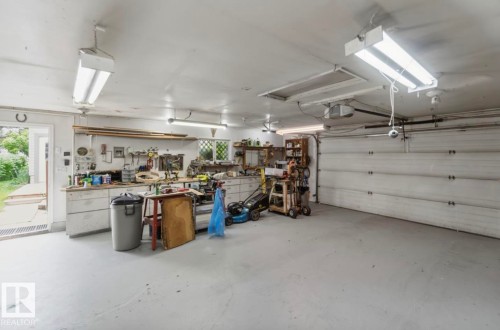 Spacious garage featuring a light gray concrete floor, white painted walls and ceiling, fluorescent overhead lighting, and a white paneled garage door - 4007 45 Street, Stony Plain, AB 