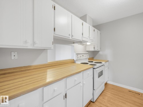 Kitchen featuring abundant white cabinetry, butcher block style countertops, a white electric range, and wood-finish flooring - 301 10528 29 Avenue, Edmonton, AB 