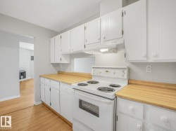 Kitchen featuring white cabinetry, wood-finish countertops, and an electric range with an overhead exhaust fan - 
