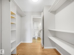 Walk-in closet featuring wood-finish flooring, white shelving units, and a bright overhead light fixture - 