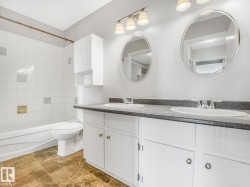 Bathroom featuring a dual-sink vanity with a dark countertop and white cabinetry - 