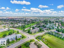 Aerial perspective showcasing a multi-story residential building with light-colored siding and a dark roof, surrounded by mature trees and manicured green spaces - 