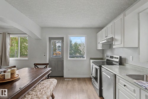 Kitchen area featuring wood-finish flooring, white cabinetry, stainless steel appliances, and a gray countertop - 1619 Welbourn Cove, Edmonton, AB 
