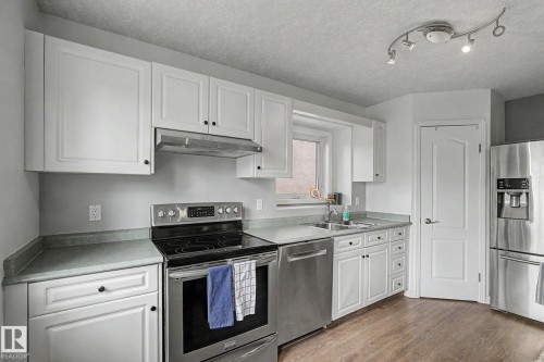 Bright kitchen featuring white cabinetry, stainless steel appliances, wood-finish flooring, and track lighting - 1619 Welbourn Cove, Edmonton, AB 