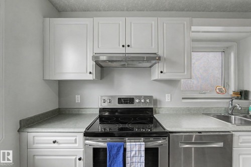 Kitchen featuring white cabinetry, stainless steel appliances, a double basin sink, and a window above the sink - 1619 Welbourn Cove, Edmonton, AB 