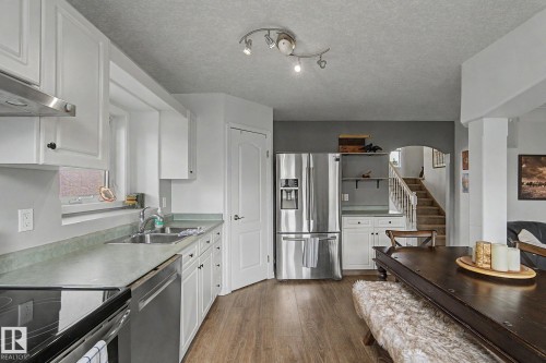 Kitchen featuring wood-finish flooring, white cabinetry, integrated stainless steel appliances, and track lighting - 1619 Welbourn Cove, Edmonton, AB 