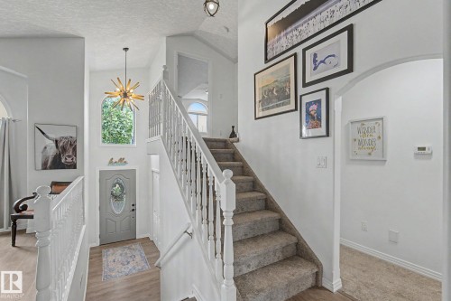 Entryway featuring a two-story foyer, a grand staircase with white banisters, a modern starburst chandelier, and an arched window - 1619 Welbourn Cove, Edmonton, AB 