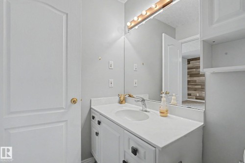Bathroom vanity featuring a white countertop with an integrated sink, a single-handle chrome faucet, and a large mirror with overhead vanity lighting - 1619 Welbourn Cove, Edmonton, AB 