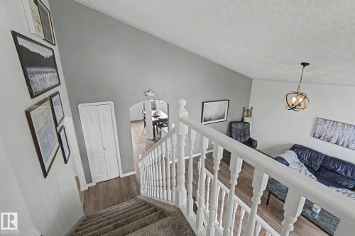 Carpeted staircase with white balustrade leading to an open-concept area featuring wood-finish flooring - 1619 Welbourn Cove, Edmonton, AB 