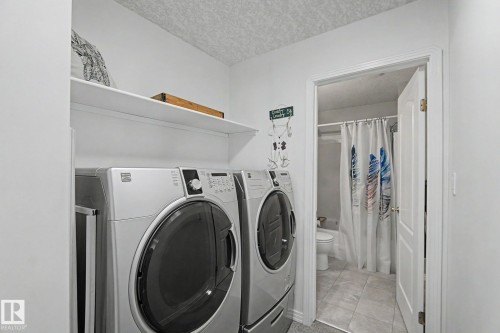 Laundry area featuring a side-by-side washer and dryer, an overhead shelf, and a white interior door - 1619 Welbourn Cove, Edmonton, AB 