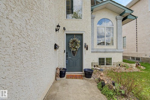 Stucco exterior featuring a prominent arched window, decorative entry door, and concrete walkway - 1619 Welbourn Cove, Edmonton, AB 
