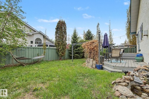 Spacious backyard featuring a multi-level wood deck, a stone water feature, a green privacy fence, and mature landscaping - 1619 Welbourn Cove, Edmonton, AB 