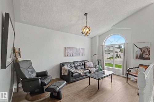 Vaulted ceiling living area featuring a large arched window, wood-finish flooring, and a decorative pendant light fixture - 1619 Welbourn Cove, Edmonton, AB 
