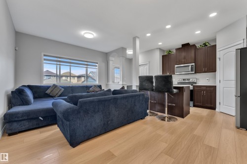 Open-concept living area featuring light wood-finish flooring, a kitchen with dark cabinetry, stainless steel appliances, a tile backsplash, and recessed lighting - 2246 54 Street, Edmonton, AB 