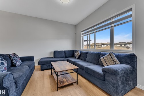 Spacious room with light wood-finish flooring, a large window featuring horizontal blinds, and a neutral wall color - 2246 54 Street, Edmonton, AB 