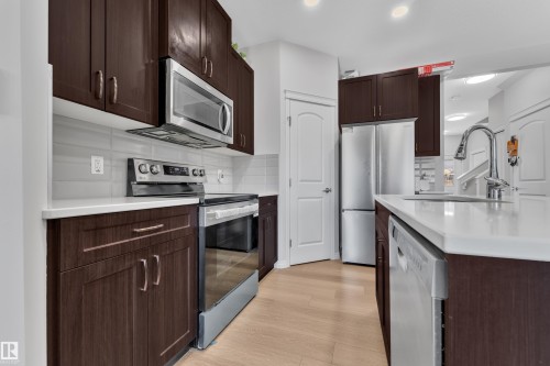 Modern kitchen featuring stainless steel appliances, dark wood-finish cabinetry, a light countertop, and light wood-finish flooring - 2246 54 Street, Edmonton, AB 
