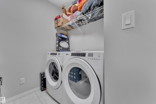 Dedicated laundry area featuring a front-loading washer and dryer set, wire shelving for storage, light gray walls, and white tile flooring - 2246 54 Street, Edmonton, AB 
