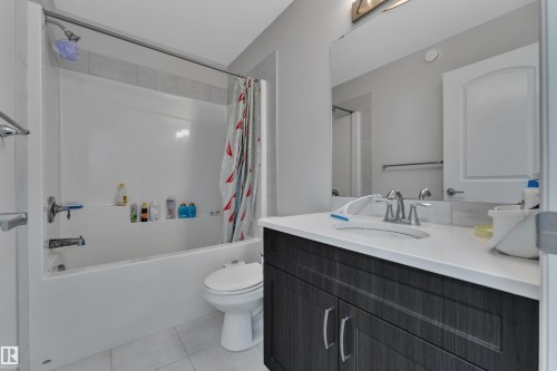 Bathroom featuring a white tub and shower combination, a dark wood-finish vanity with a light countertop, a rectangular mirror, and white tile flooring - 2246 54 Street, Edmonton, AB 