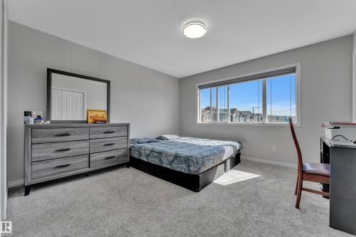 Carpeted bedroom featuring a wide window, light gray walls, white trim, and a ceiling-mounted light fixture - 2246 54 Street, Edmonton, AB 