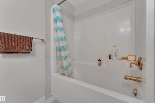 White bathtub and shower combination featuring a built-in shelf, brass-finish fixtures, and light gray tile surround - 2246 54 Street, Edmonton, AB 