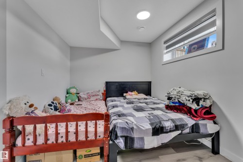 Bedroom with light gray walls, wood-finish flooring, a contemporary flush-mount ceiling light, and a horizontal window with a white frame - 2246 54 Street, Edmonton, AB 