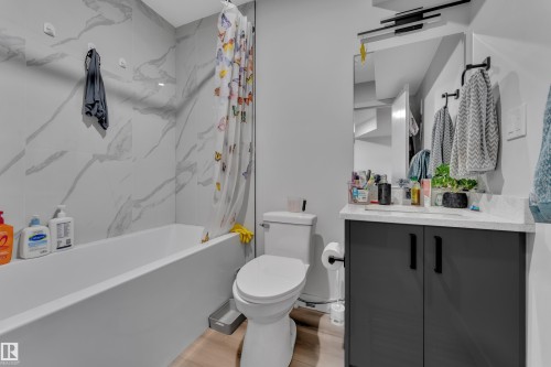 Bathroom featuring a white bathtub, large format marble-look wall tiles, a white toilet, and a vanity with dark cabinetry, a light-colored countertop, and a rectangular mirror - 2246 54 Street, Edmonton, AB 
