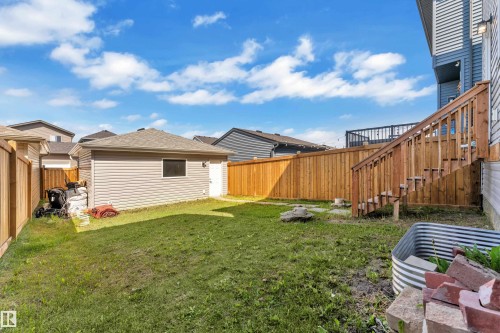 Spacious backyard featuring a detached garage with vinyl siding, a wooden privacy fence, natural grass, and a wooden staircase leading to an upper deck - 2246 54 Street, Edmonton, AB 