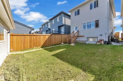 Rear exterior of a two-story residence featuring light gray siding, multiple windows, and a ground-level walkout door with a wood staircase - 2246 54 Street, Edmonton, AB 