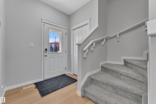 Entryway featuring a white paneled door with glass inserts, wood-finish flooring, light grey walls, and a carpeted staircase with white trim and railing - 2246 54 Street, Edmonton, AB 