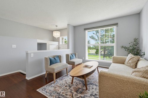 Spacious living area featuring rich wood-finish flooring, a large window, a partial wall, and a built-in light fixture - 126 2051 Towne Centre Boulevard, Edmonton, AB 