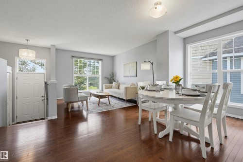 Open concept living and dining areas featuring dark wood-finish flooring, light gray wall paint, white trim, and multiple large windows - 126 2051 Towne Centre Boulevard, Edmonton, AB 