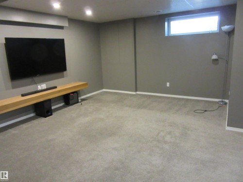 Spacious room featuring neutral carpeting, a high-mounted window, recessed ceiling lighting, and a floating wood-finish media shelf - 64 Heatherglen Close, Spruce Grove, AB 