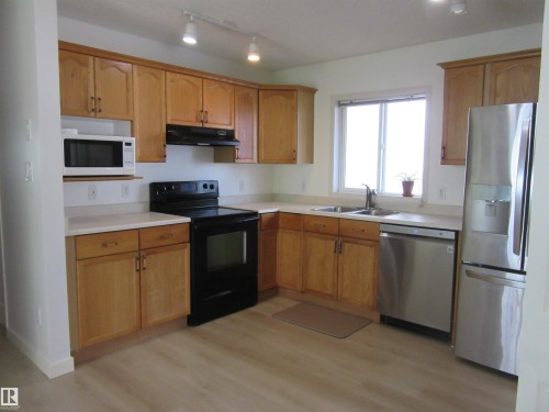 Kitchen featuring wood-finish cabinetry, solid surface countertops, stainless steel appliances, and wood-look flooring - 64 Heatherglen Close, Spruce Grove, AB 
