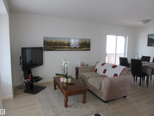 Open-concept living area with light wood-finish flooring, white walls, and a sliding glass door leading to an outdoor deck - 64 Heatherglen Close, Spruce Grove, AB 