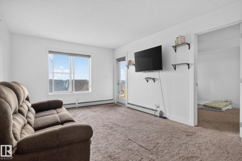 Spacious living area featuring neutral carpeting, white walls, a large window, and a door leading to an outdoor space - 415 111 Watt Common, Edmonton, AB 