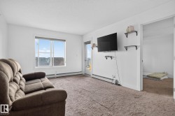 Spacious living area featuring neutral carpeting, white walls, a large window, and a door leading to an outdoor space - 