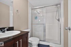 Bathroom featuring a dark wood-finish vanity with an undermount sink, dark stone countertop, and a shower with sliding glass doors - 