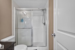 Shower enclosure with sliding glass doors, white subway tile surround, chrome fixtures, and a textured ceiling - 