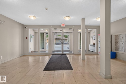 Spacious entry foyer featuring light-toned tile flooring, neutral wall paint, overhead flush-mount lighting, and floor-to-ceiling glass paneling at the entrance - 415 111 Watt Common, Edmonton, AB 