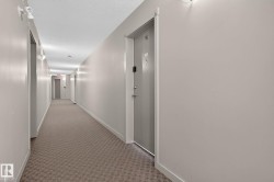 Hallway featuring neutral-toned walls, patterned carpet flooring, and sconce lighting fixtures - 