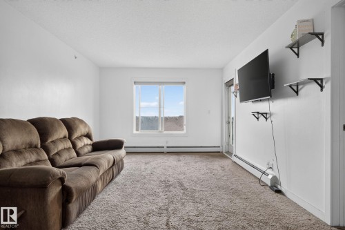 Bright living space featuring neutral carpeting, a large window, and a door providing exterior access - 415 111 Watt Common, Edmonton, AB 