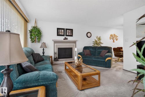Living area featuring a fireplace with a light-colored mantel, light gray carpeting, and white walls - 4712 131 Avenue Nw, Edmonton, AB 