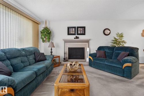 Living area featuring a fireplace with a light-toned mantel, a fireplace screen, and light-colored wall-to-wall carpeting - 4712 131 Avenue Nw, Edmonton, AB 