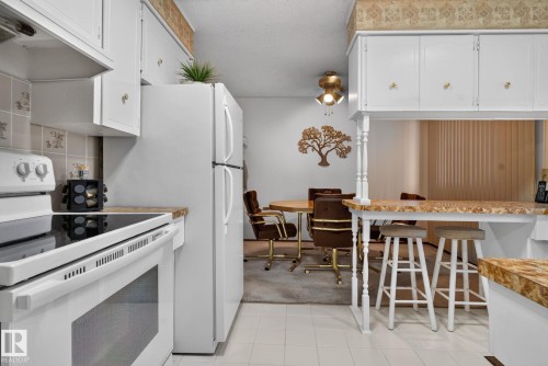 Kitchen featuring white cabinetry with gold-toned hardware, white appliances, and patterned countertops - 4712 131 Avenue Nw, Edmonton, AB 
