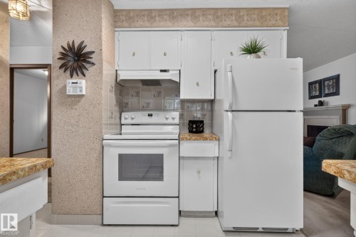 Kitchen featuring white appliances, a patterned tile backsplash, white cabinetry, and light-toned countertops - 4712 131 Avenue Nw, Edmonton, AB 