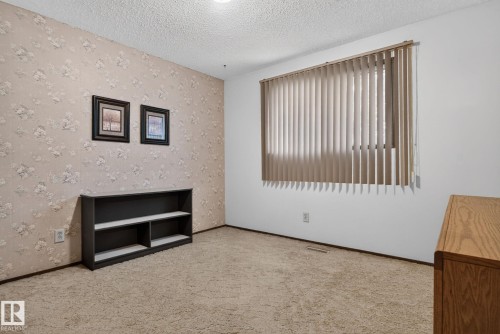 Room featuring textured wallpaper, carpet flooring, and a large window with vertical blinds - 4712 131 Avenue Nw, Edmonton, AB 