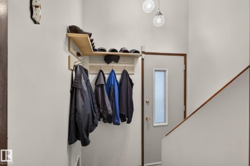 Entryway featuring a light wood-finish built-in coat rack with integrated shelving, two textured glass pendant light fixtures, and a white interior door with a frosted glass insert - 4712 131 Avenue Nw, Edmonton, AB 