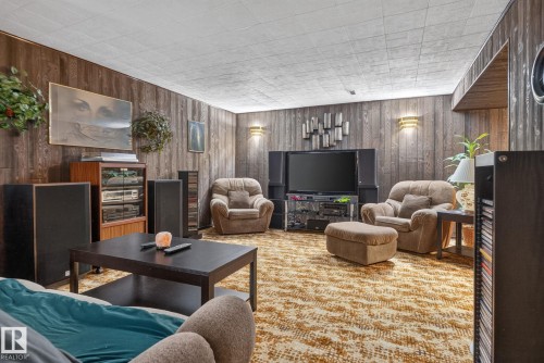 Recreation room featuring wood-finish wall paneling, textured ceiling, wall-mounted sconce lighting, and patterned carpeting - 4712 131 Avenue Nw, Edmonton, AB 